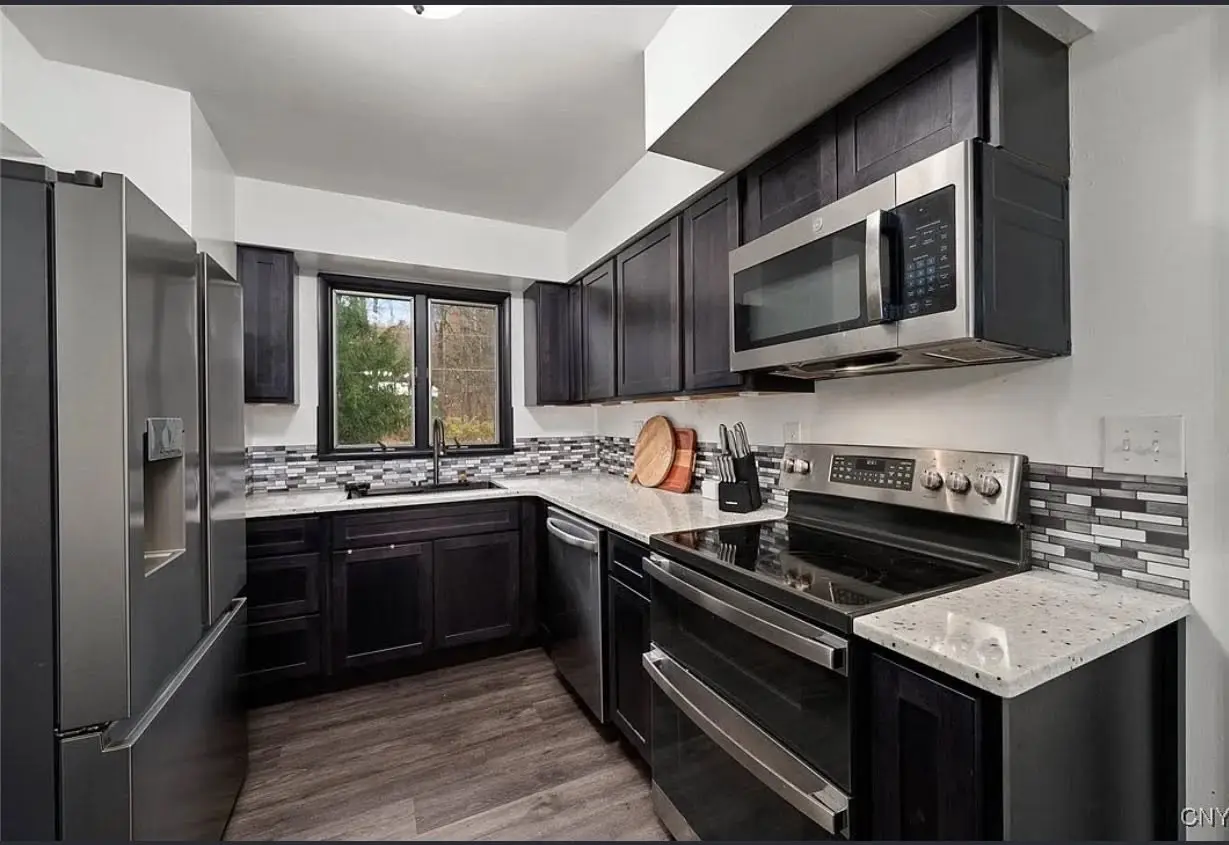 Remodeled kitchen with dark shaker cabinets, stone countertops, and stainless appliances