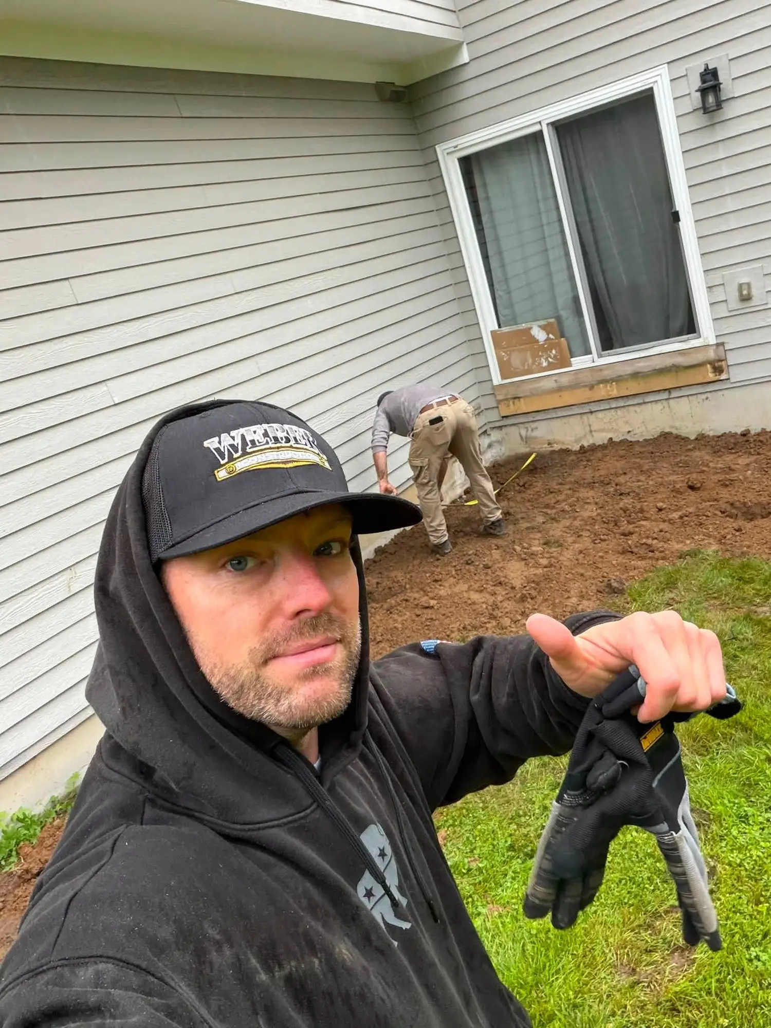Matt Weber, owner of Weber Construction, in a Weber Construction cap on a job site while his crew grades soil along the side of a home